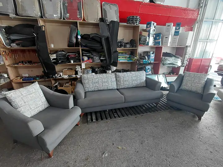 Atölyede yeniden döşenmiş gri kanepe ve iki berjerden oluşan koltuk takımı